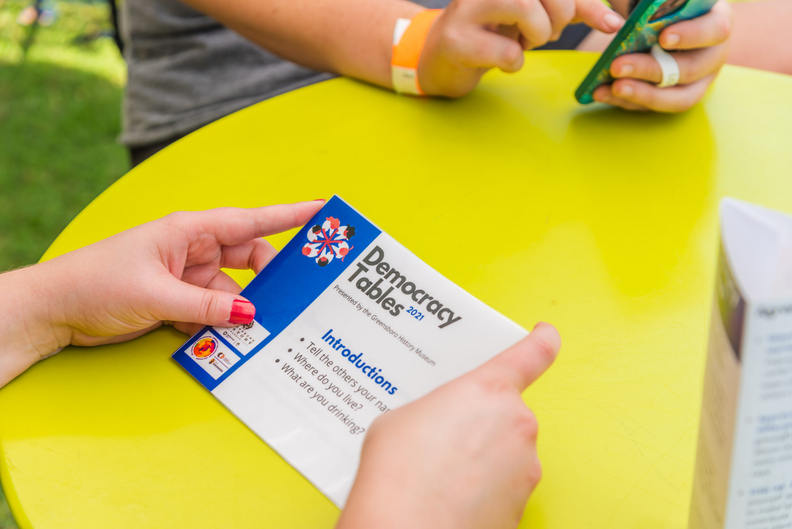 Hands holding a card that says "Democracy Tables" on it